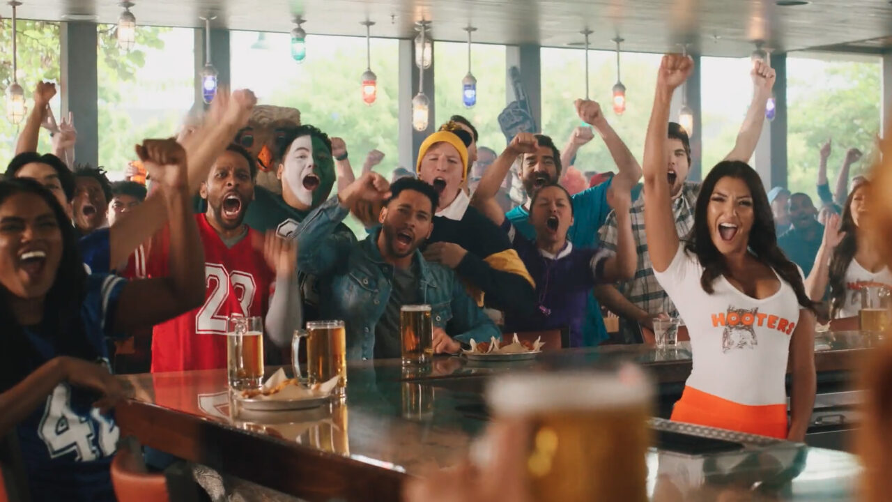 Group of people in a Hooters raising their hands in excitement.